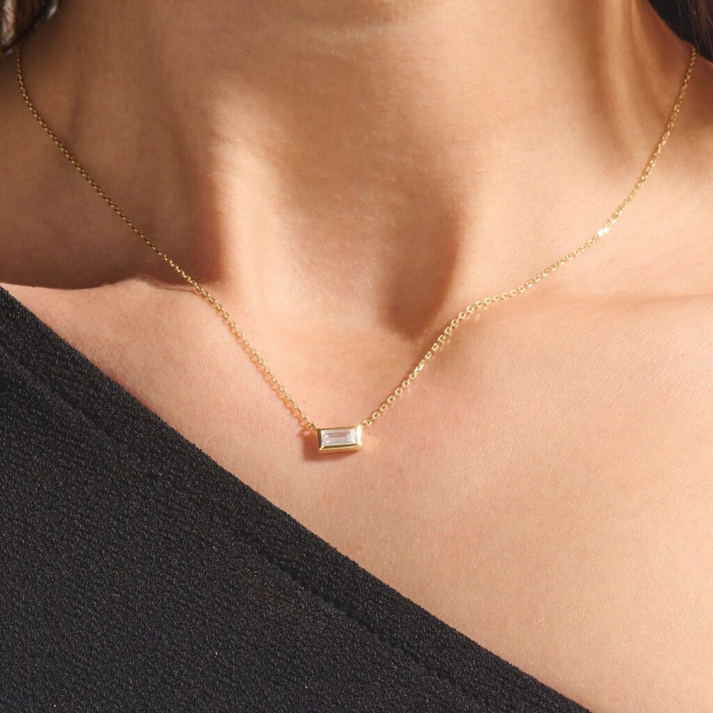 Minimalist gold necklace with a single baguette-cut diamond pendant worn close to the collarbone